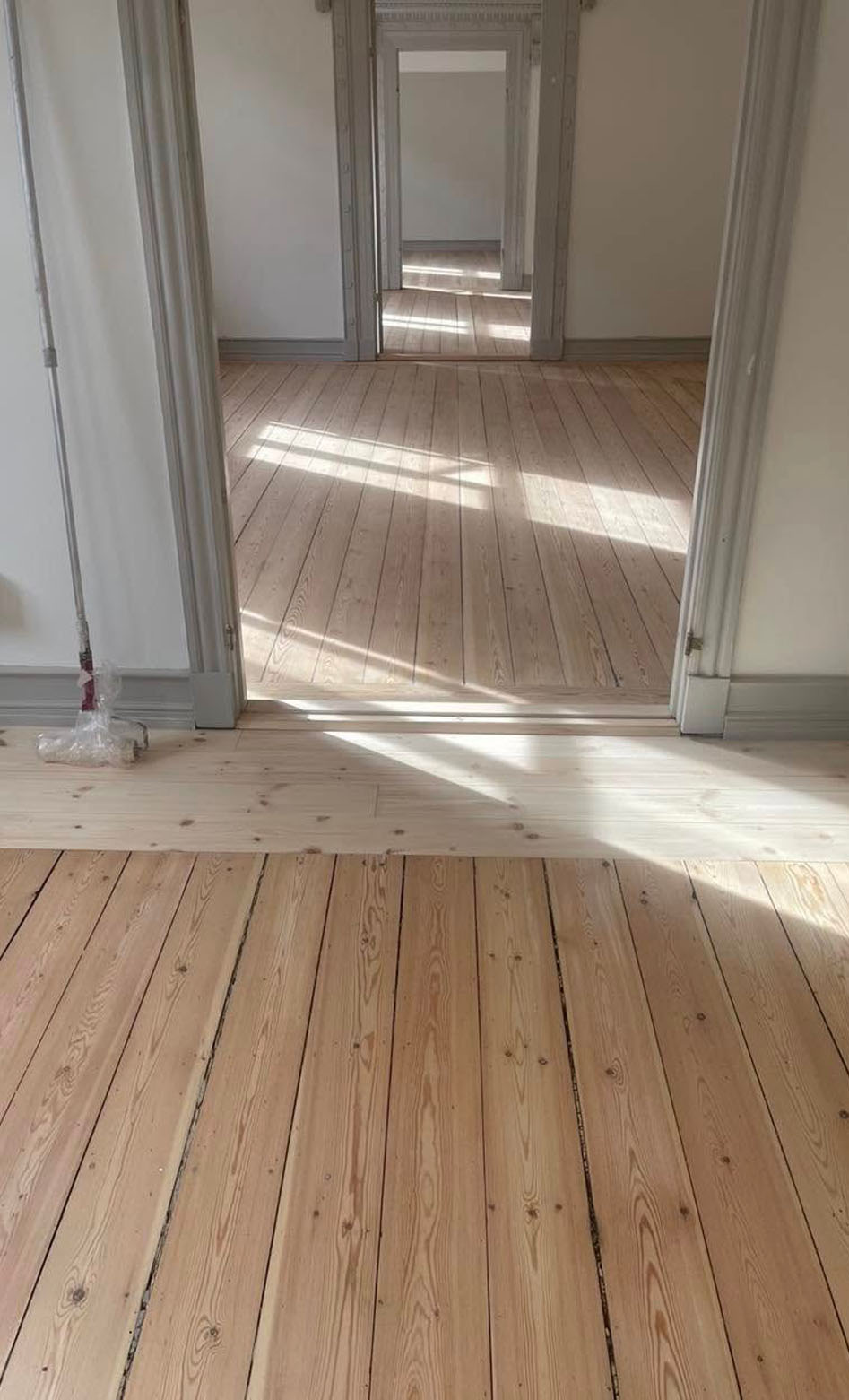 Efter-billede af det samme trægulv, som nu er nyslebet, lyst og smukt efterbehandlet. Dørtrinnet mellem stuerne er også nyslebet.