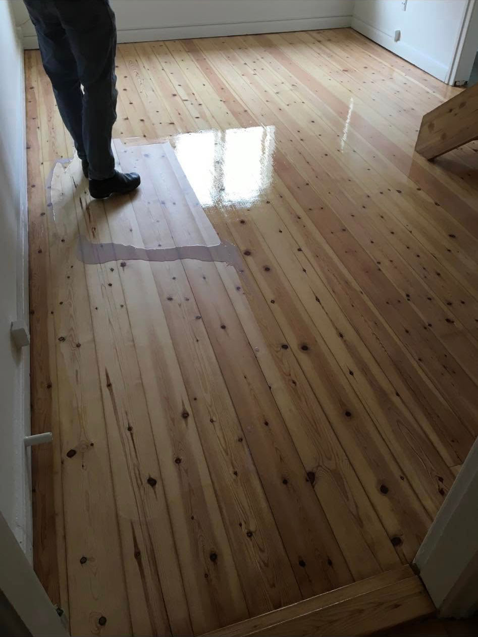 Påføring af lakbehandling på et nyslebet fyrretræsgulv, som giver en stærk og blank overflade, der er nem at rengøre.