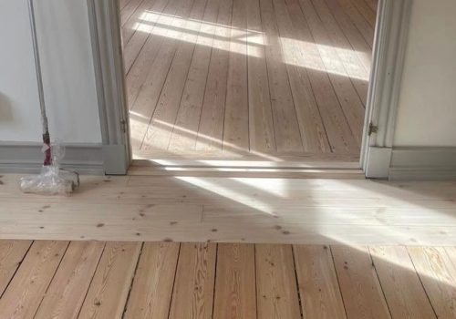 Efter-billede af det samme trægulv, som nu er nyslebet, lyst og smukt efterbehandlet. Dørtrinnet mellem stuerne er også nyslebet.
